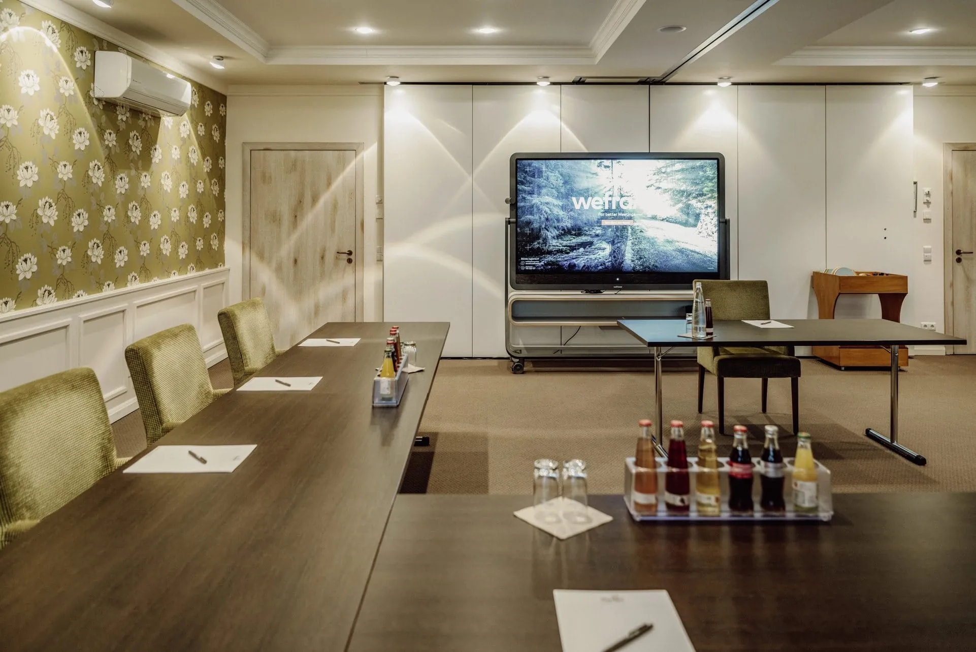 Moderner Tagungsraum mit gr&uuml;nen Polsterst&uuml;hlen und Cannyboard f&uuml;r hybride Meetings