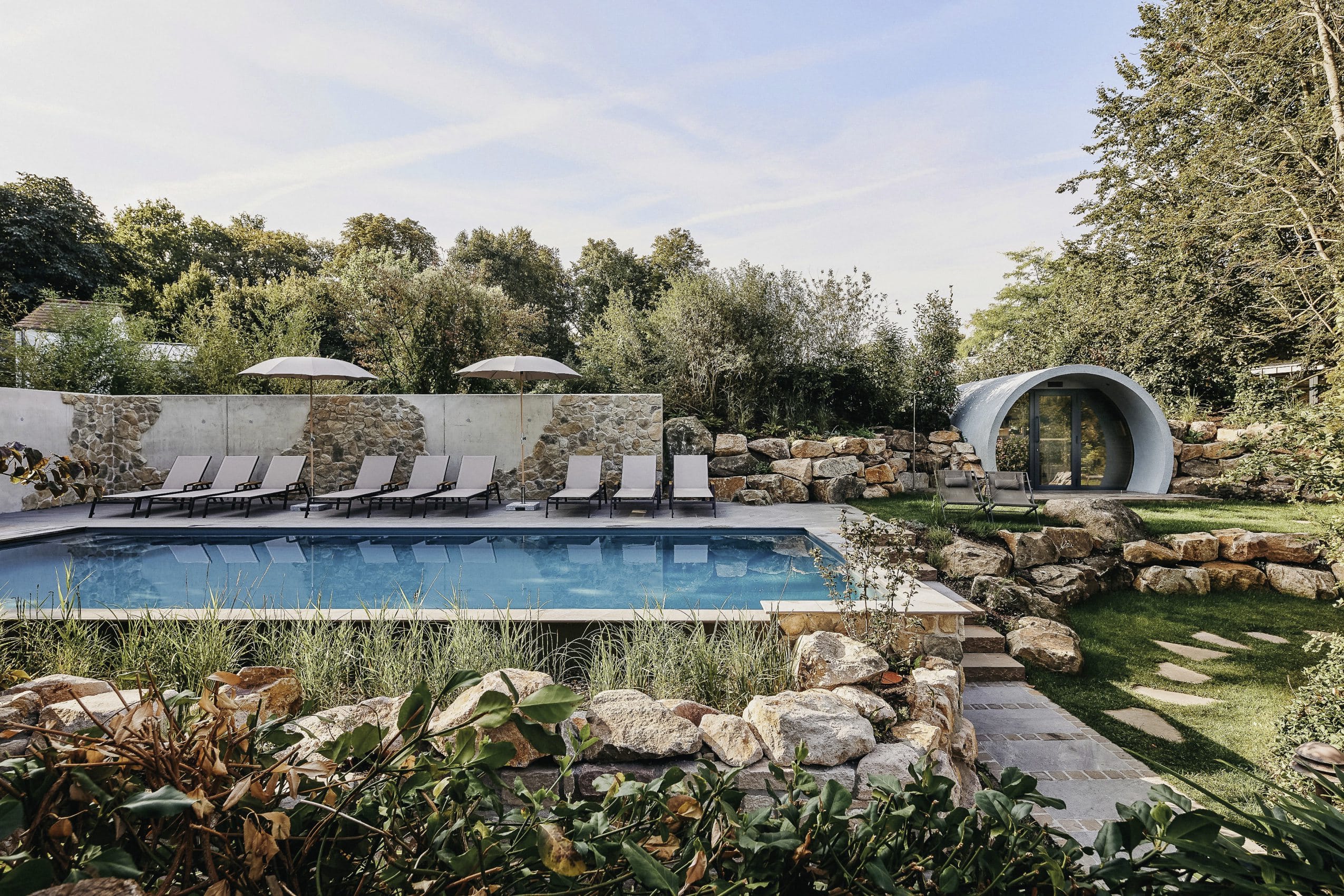 Outdoorpool mit Liegen und Sonnenschirmen im Naturgarten mit Bruchsteinen im Landhotel Voshövel
