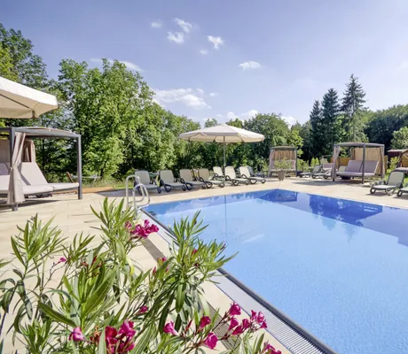 Außenpool mit Ruheliegen und hellen Sonnenschirmen hinter Oleanderbusch