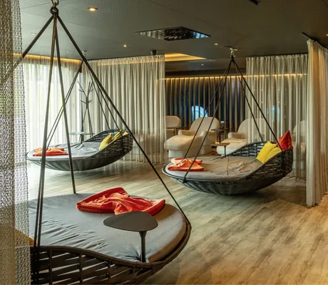 Hängekorbnester mit orangen Decken im Spabereich neben Wand mit Waldtapete