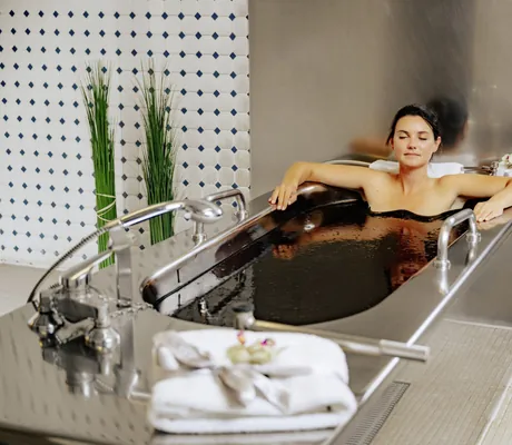 dunkelhaarige Frau liegt in metallener Wanne und absolviert ein Moorbad