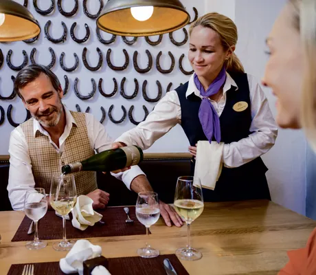 Servicemitarbeiterein in schwarzer Weste schenkt Paar im Restaurant Weißwein ein