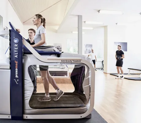 Frau mit Zopf trainiert unter Anleitung eines Personal Trainers auf einem Ant-Gravity-Gerät