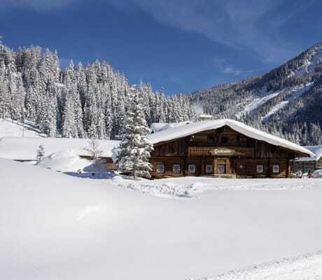 Gnadenalm-Holzhütte im tiefen Schnee mit Bergen im Hintergrund