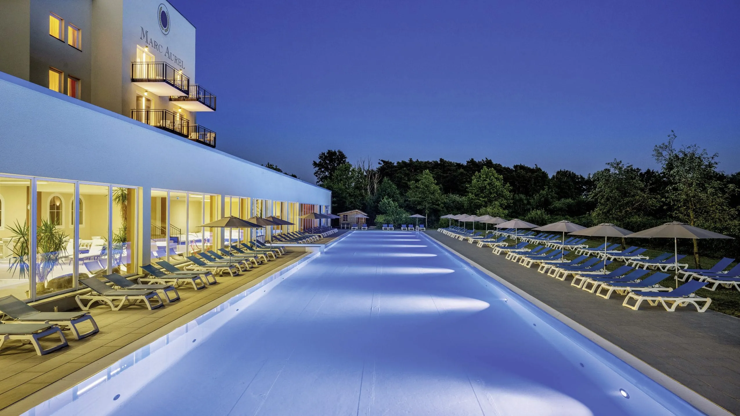 langer Außenpool mit Liegen und Sonnenschirmen bei Nacht im Marc Aurel