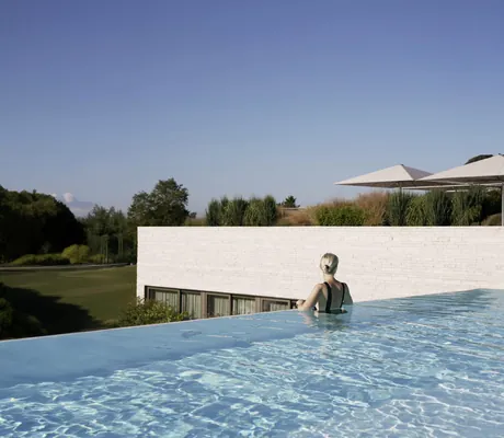 blonde Frau in schwarzem Badeanzug schaut vom Infinitypool aus auf den Golfplatz