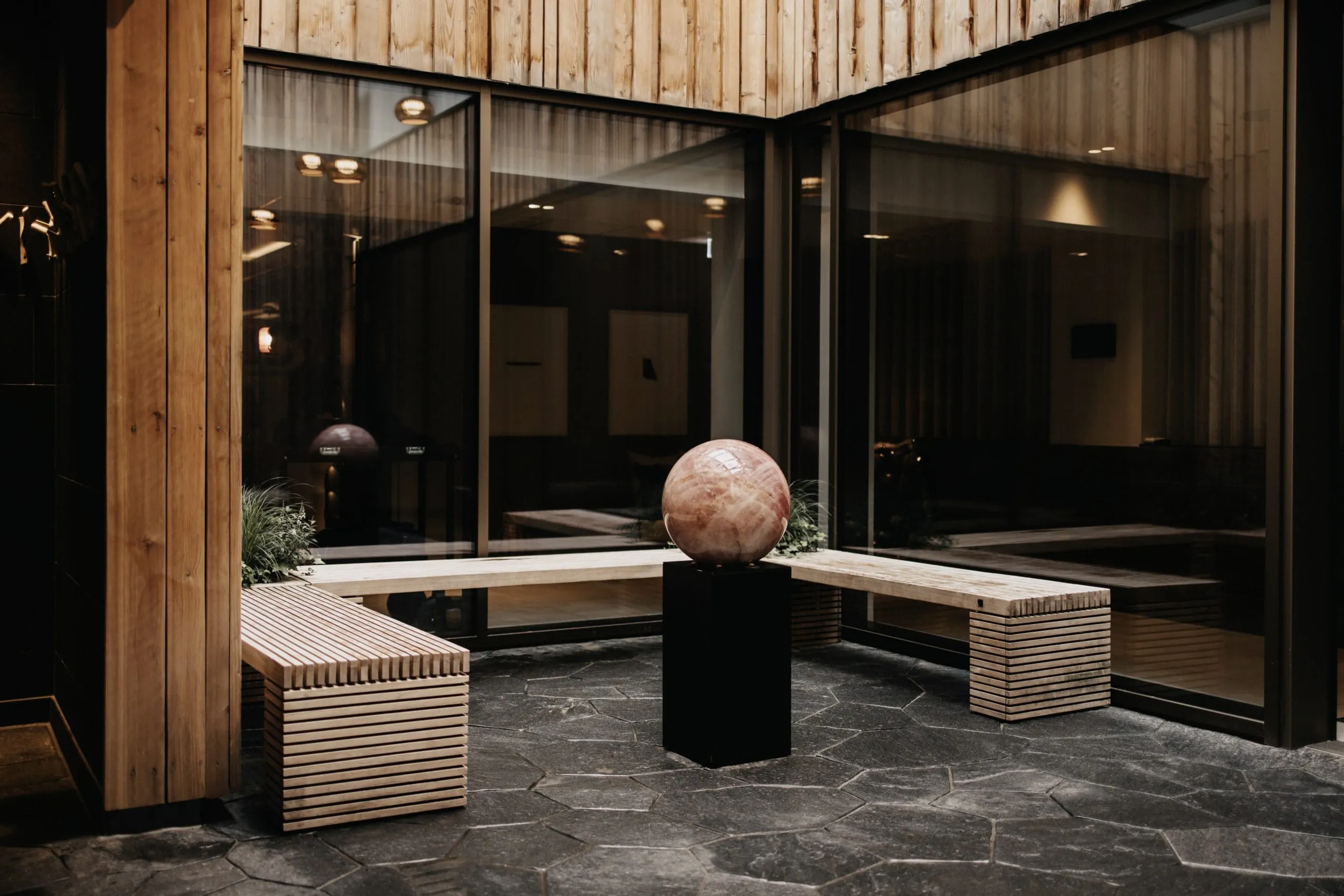 r&ouml;tliche Marmorkugel auf schwarzem Sockel vor Holzbank im Spabereich