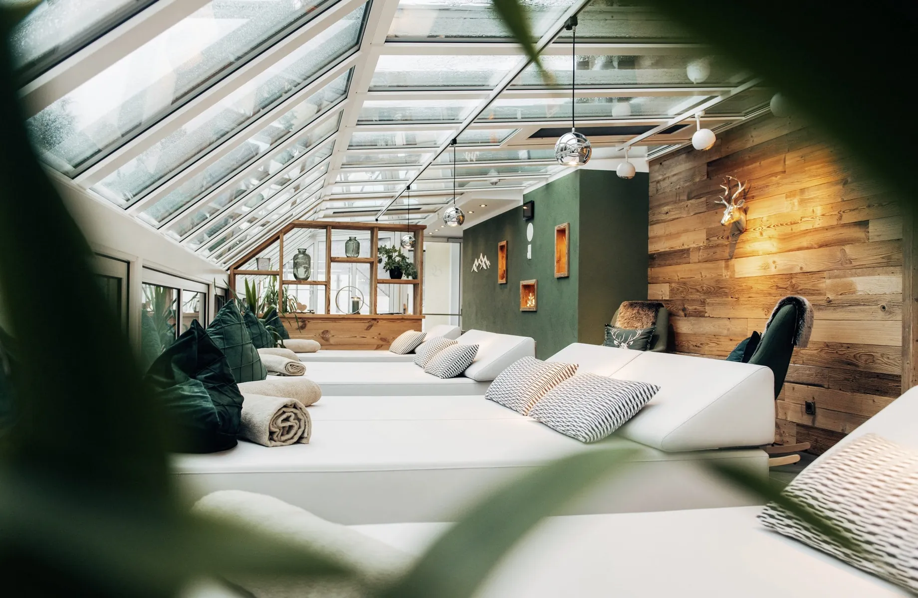 Ruheraum mit Liegen vor grüner Wand und grünen Kissen unter einem Glasdach