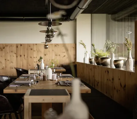 Restaurant im Hotel Pfösl mit Holztischen, Ledersesseln und Kräutern in Vasen am Rand