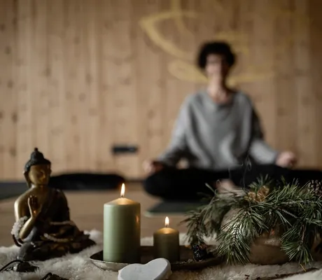 Frau Zelger sitzt im Yogasitz hinter zwei grünen Kerzen und einer Buddhafigur im Yogaraum