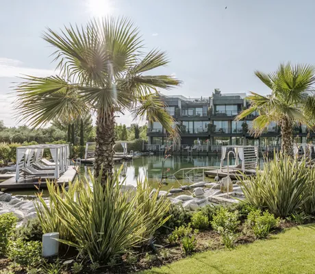 Gartenanlage des Quellenhof Luxury Resort Lazise mit Naturbadeteich und Palmen vor der Hotelfassade