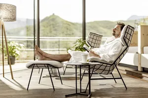 Mann in weißem Bademantel liegt bei einer Tasse Tee im Ruhesessel