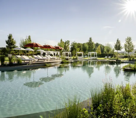 Naturbadeteich mit weißen Daybeds und roten Sonnenschirmen in der strahlenden Sonne