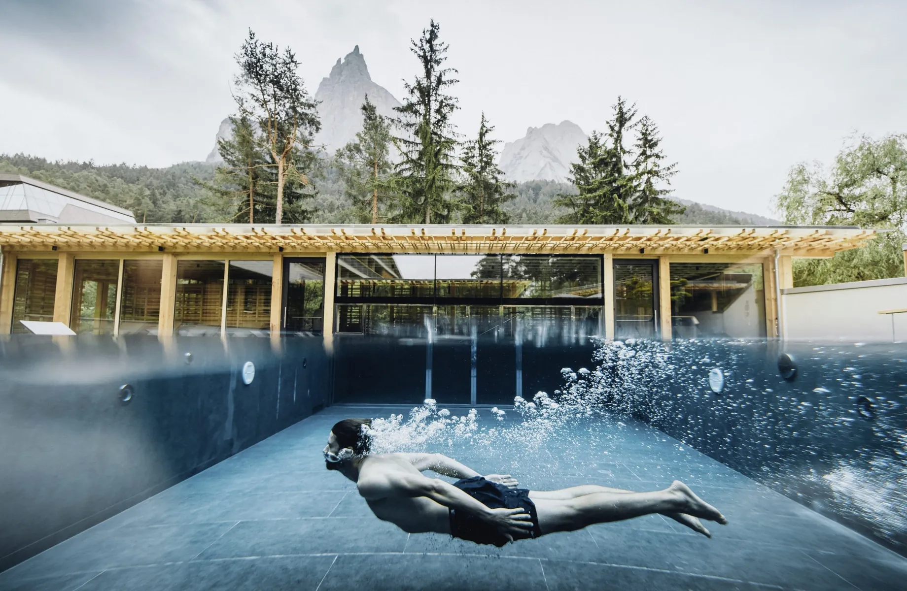 Mann in Badehose unter Wasser im Outdoorpool des Sensoria Dolomites mit Blick auf den Schlern