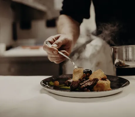 Koch träufelt aus einer Kasserole heiße Soße auf ein auf dem Teller angerichtetes Essen