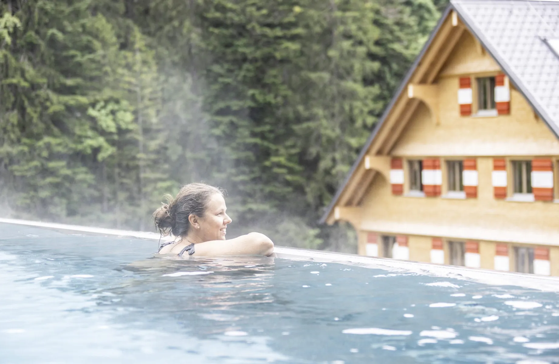 Frau am Beckenrand des Outdoorpool im Berghaus Schröcken