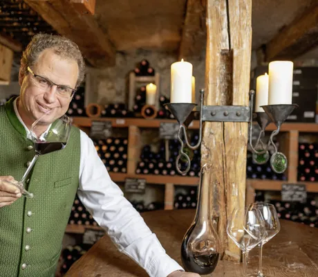 Inhaber des Böglerhof in grüner Trachtenweste hält Rotweinglas in die Kamera