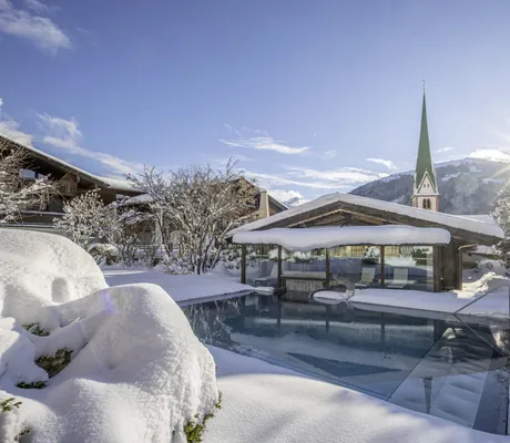 Blick auf Spabereich des Böglerhof mit Außenpool in tiefem Schnee