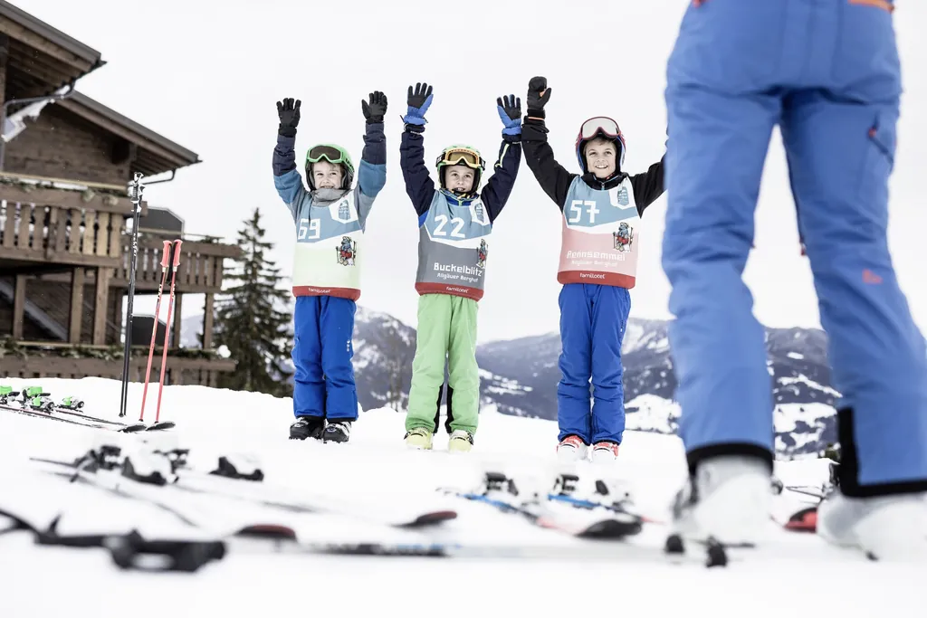 drei Kinder in Schneeanzügen mit Startnummern reißen die Hände in die Höhe im Allgäuer Berghof