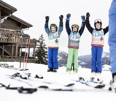 drei Kinder in Schneeanzügen mit Startnummern reißen die Hände in die Höhe im Allgäuer Berghof
