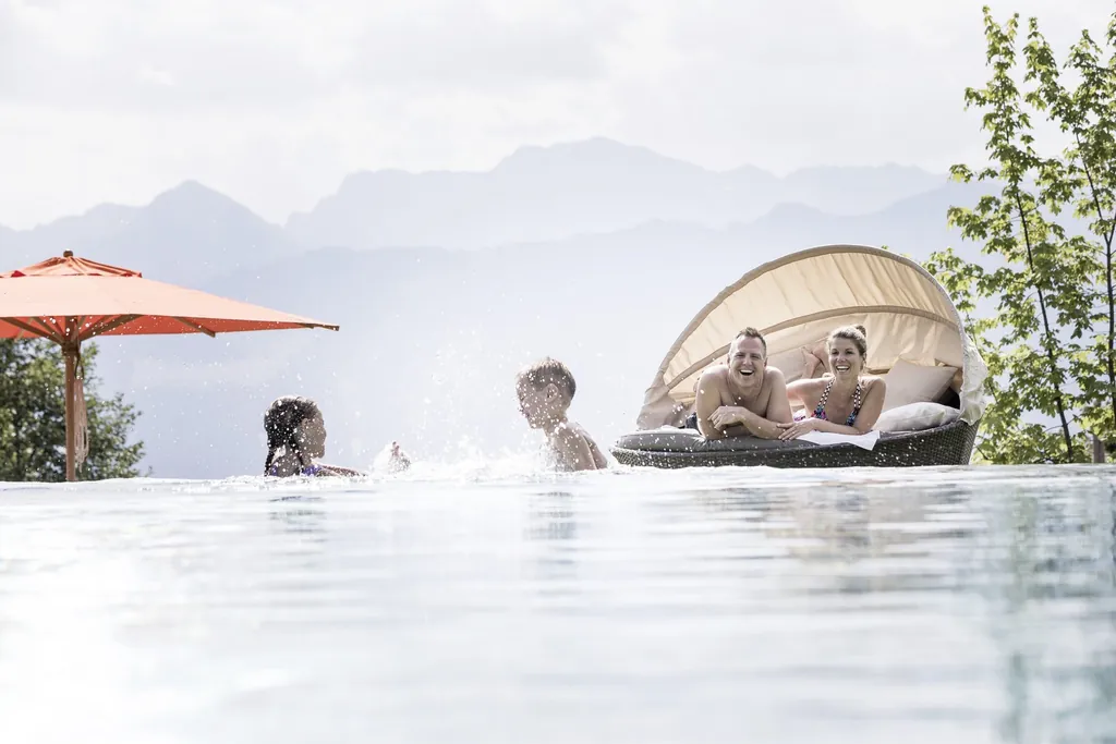 Pärchen liegt im Ruhenest, während die Kinder im Outdoorpool des Allgäuer Berghof plantschen