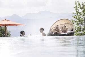 Pärchen liegt im Ruhenest, während die Kinder im Outdoorpool des Allgäuer Berghof plantschen