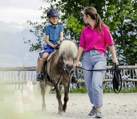 Frau in pinkem Shirt führt Pony mit Jungen im Allgäuer Berghof