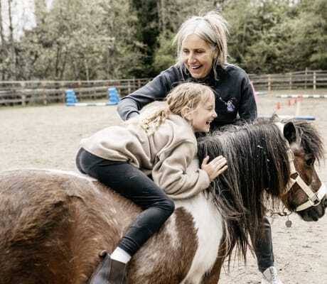 Susi Nestl hält ein Pony, auf dem ein Mädchen ohne Sattel sitzt au dem Pferdehof im Hotel Familiamus