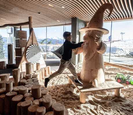 Kind springt im Zauberlabor Sandplatz auf die Holzfigur Magolix zu im Hotel Familiamus