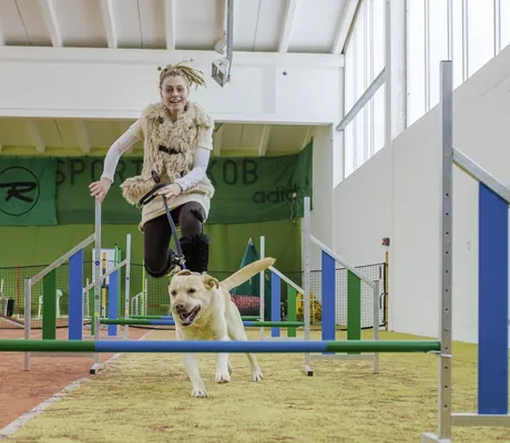 Junge Frau springt mit ihrem Hund über ein Hindernis im Agility-Parcours