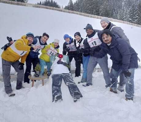 Teambuilding Gruppenaufnahme mit liegendem bekleidetem Schneemann auf Stuhl im Berghaus Schröcken