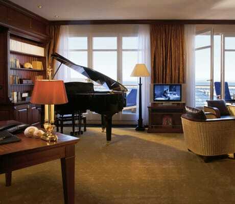 Zimmer mit Meerblick, Piano, Bibliothek und Korbsesseln mit Sitzlederbezug in der Yachthafenresidenz Hohe Düne
