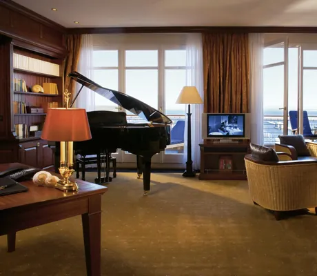 Zimmer mit Meerblick, Piano, Bibliothek und Korbsesseln mit Sitzlederbezug in der Yachthafenresidenz Hohe Düne
