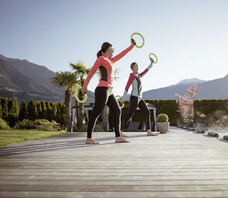 zwei Frauen mit Gewichten stehen am Außenpool des La Maiena Meran Resortund machen Übungen
