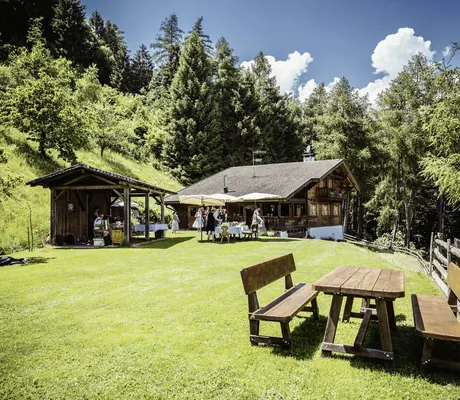 Hütte der Flatscheralm mit Holzbank und Musikern in einem Unterstand