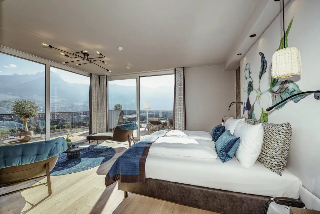 Zimmer mit riesigen Panoramafenstern und Blick auf das Meraner Land und blauem runden Teppich im La Maiena Meran Resort