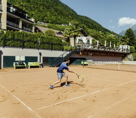 Mann in blauem T-Shirt spielt Tennis auf dem Außen-Sandplatz im La Maiena Meran Resort