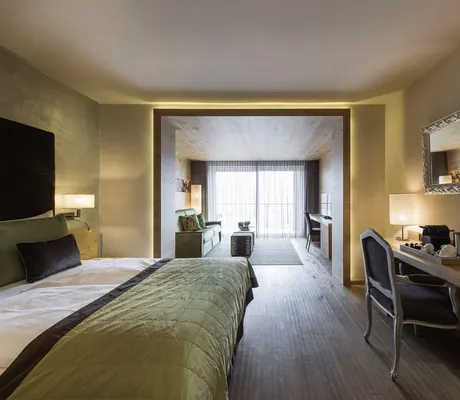 großes Zimmer mit blauem Bettüberwurf und goldgerahmtem Spiegel im La Maiena Meran Resort