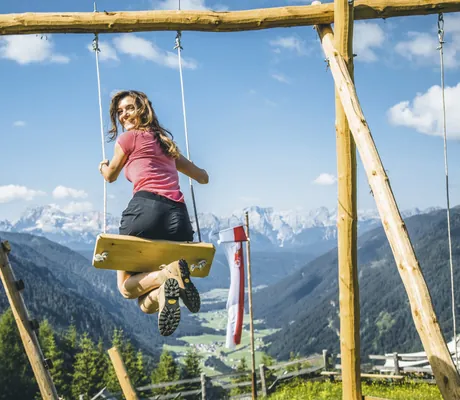 Frau mit rotem T-Shirt schaukelt auf riesiger Schaukel in Richtung Dolomiten im Hotel Quelle