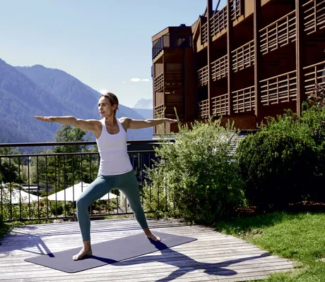 Frau in weißem T-Shirt macht Yoga auf einer Plattform vor der Fassade des Hotel Quelle