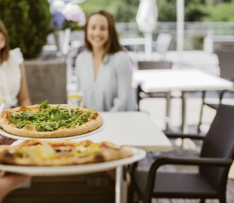 Mann trägt zwei Pizzen an den Tisch zu zwei Frauen im Reiters Allegria Hotel