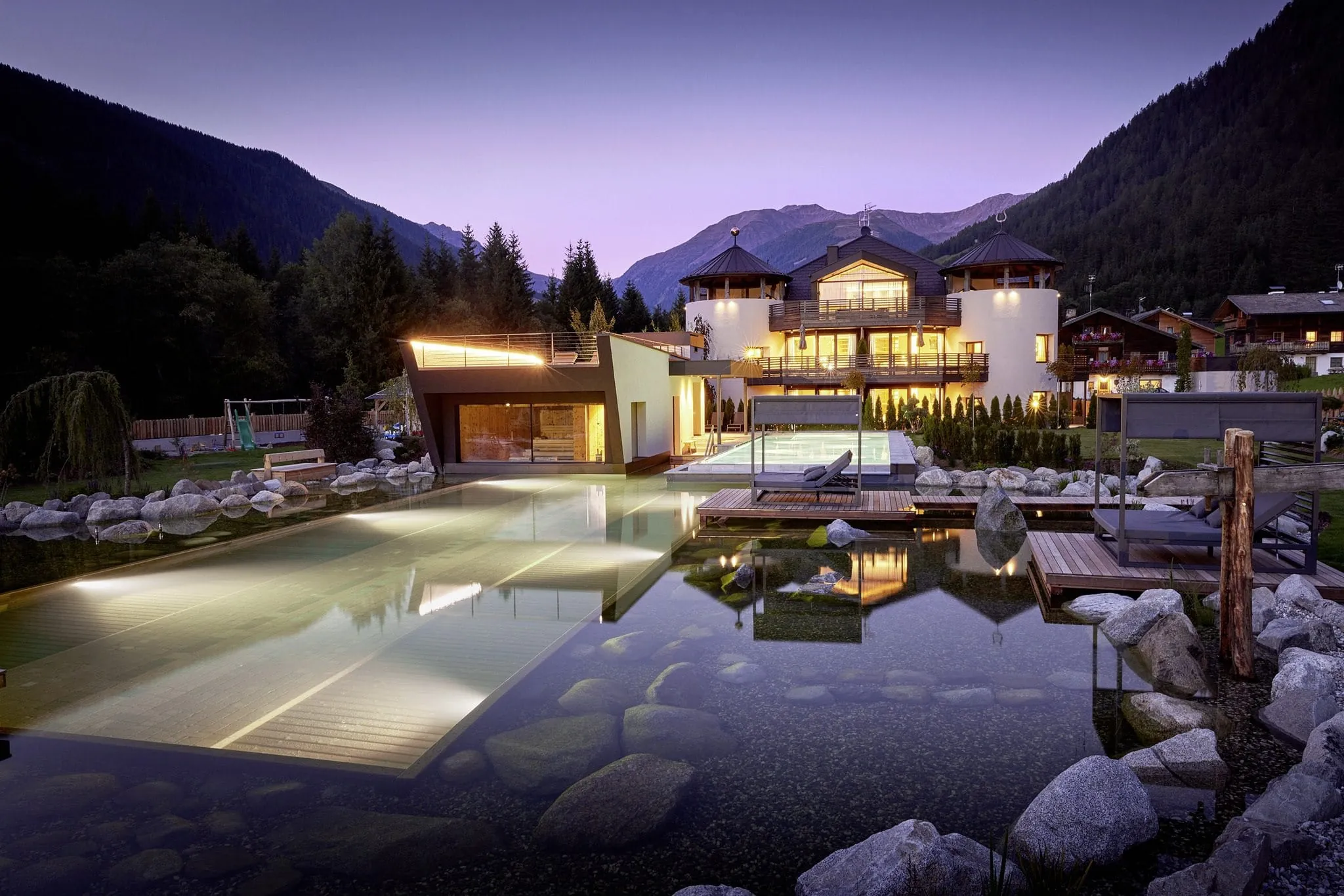 Außenaufnahme des FONTIS luxury spa lodge mit Pool und Teich am Abend