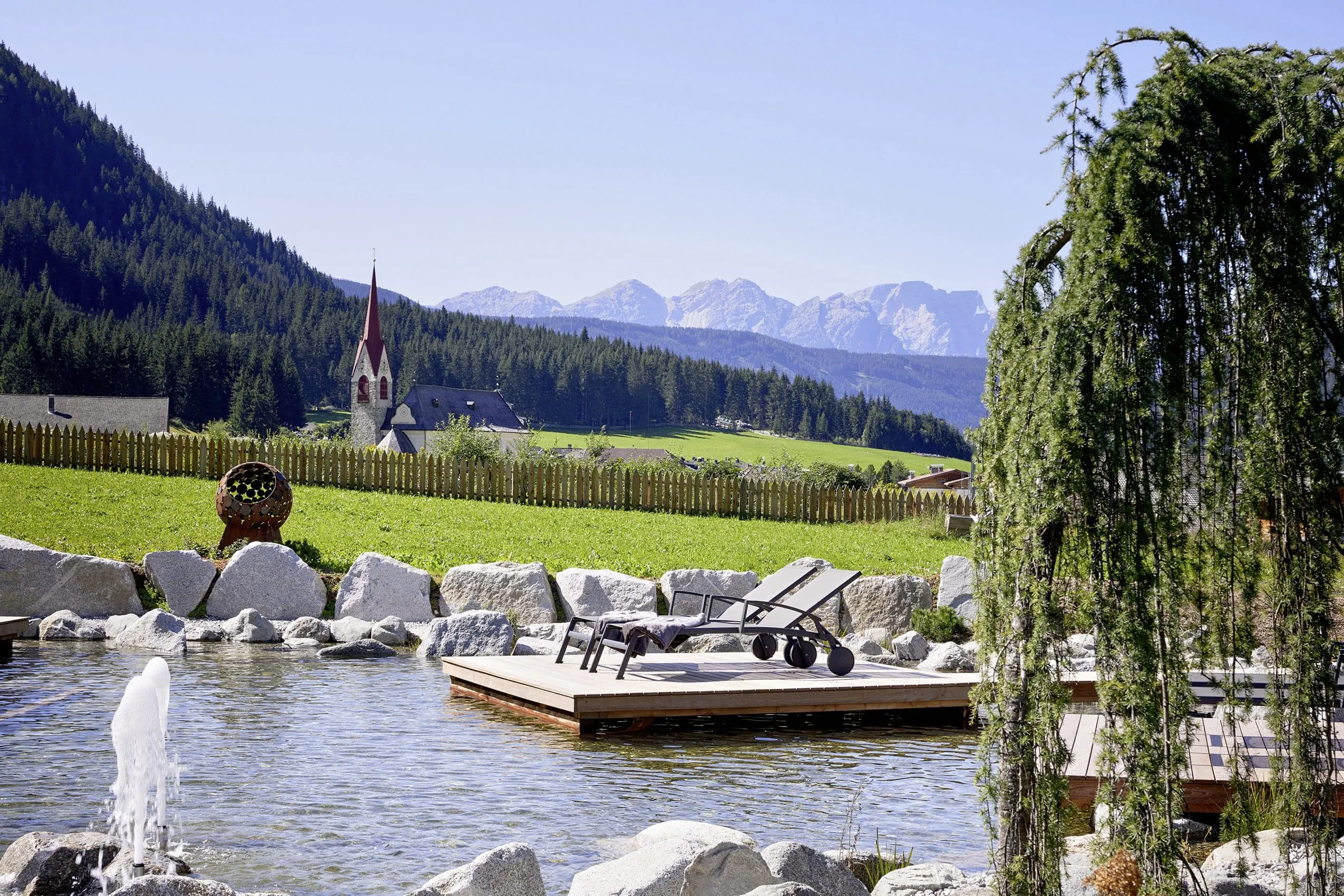 Holzponton am Teich des FONTIS luxury spa lodge mit Blick auf die Kirche