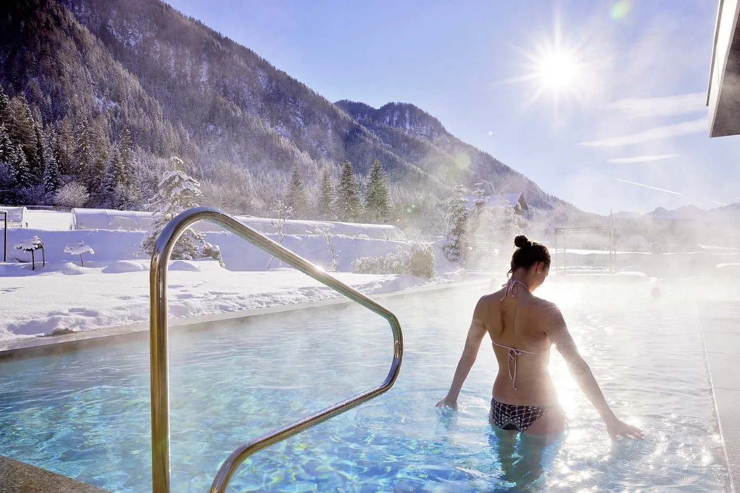 Frau im Bikini steht im Winter im Außenpool des FONTIS luxury spa lodge mit Blick auf die Südtiroler Berge