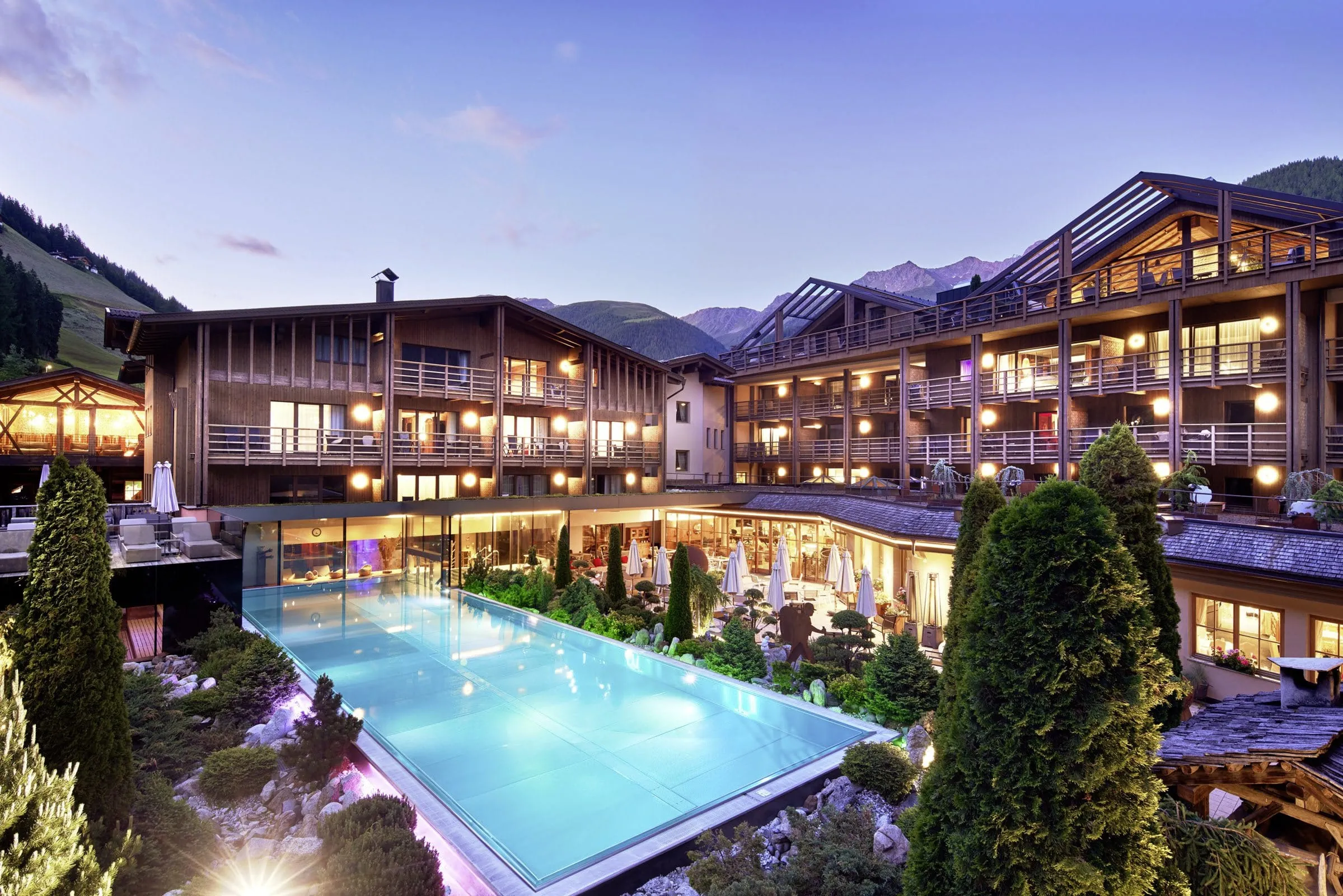 Gesamtansicht des Hotel Quelle mit Outdoorpool und Rooftop-Spa in der Dämmerung