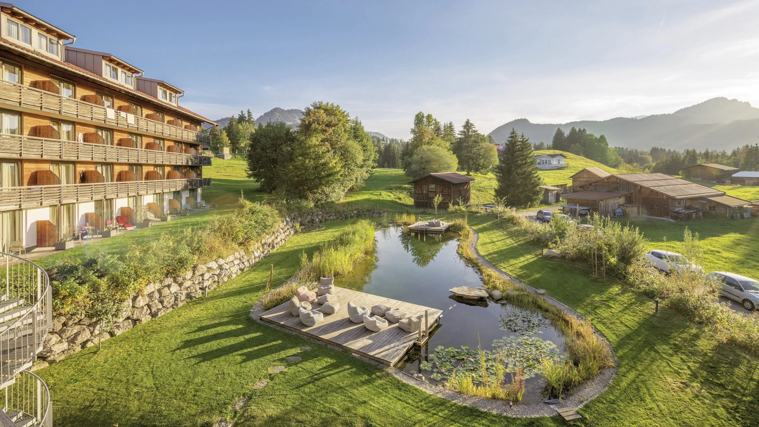 Au&szlig;enfassade des Wellnesshotel Oberstdorf im Allg&auml;u mit Naturbadesee im Vordergrund