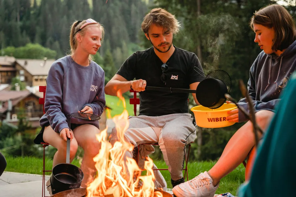 Einige Jugendliche sitzen beim Berghaus Schröcken ums Lagerfeuer und bereiten sich ein Essen zu