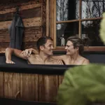 Paar in Holz-Badezuber auf der Terrasse der Alpzitt Chalets