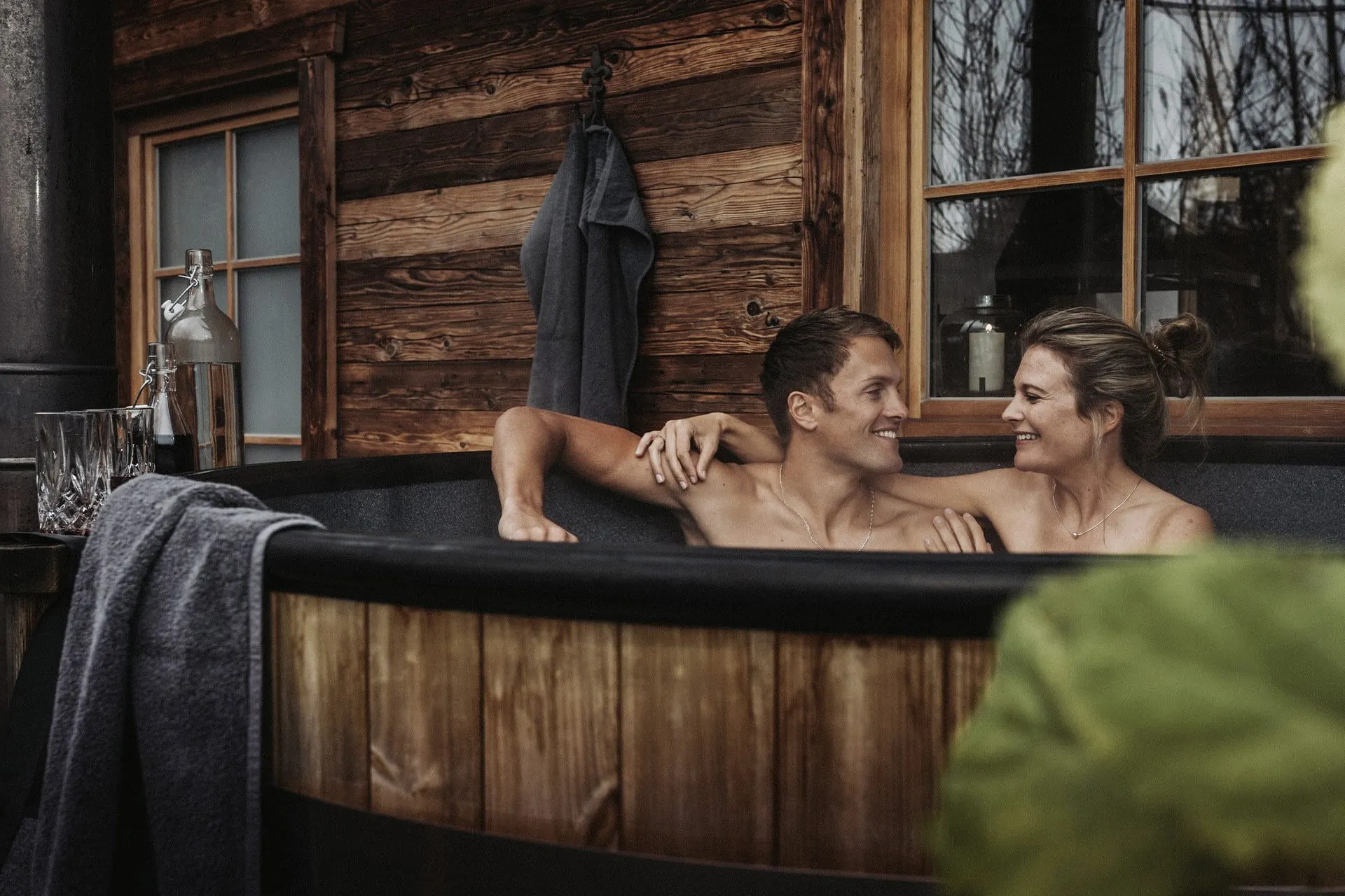 Paar in Holz-Badezuber auf der Terrasse der Alpzitt Chalets