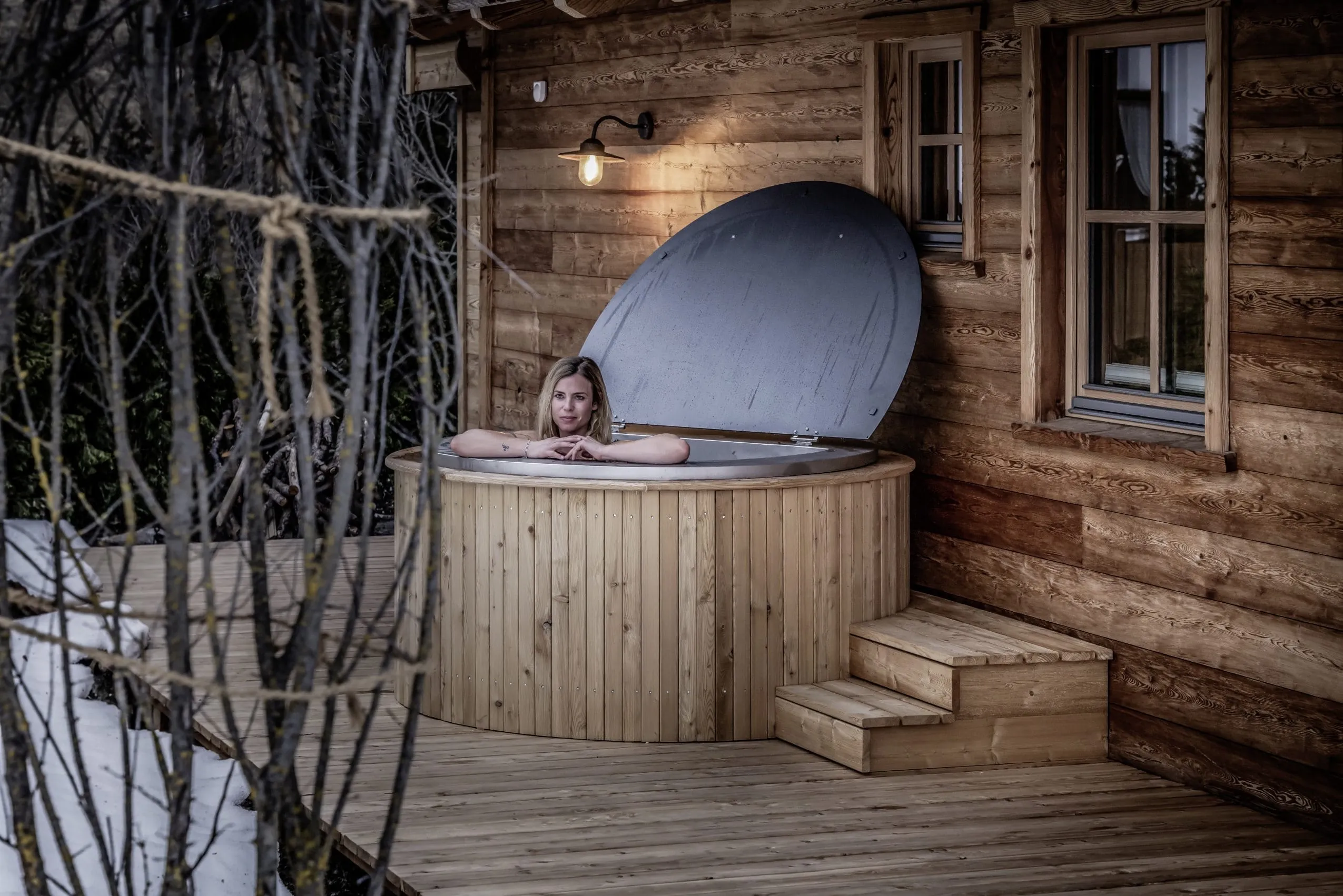 blonde Frau in Holz-Badezuber auf der Terrasse des Benglerwald Chaletdorf